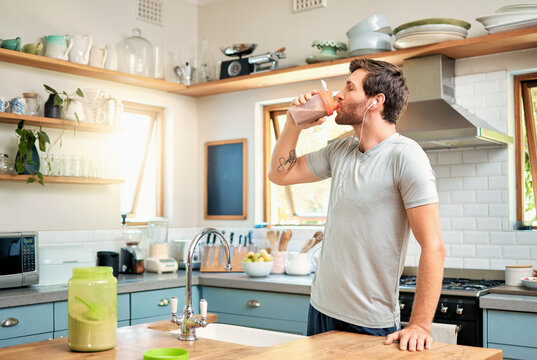 Wellness, earphones and man in kitchen with protein shake, whey recipe or smoothie for gut health. Fitness, person and audio tech in home with supplement drink, nutrition and exercise tips in podcast
