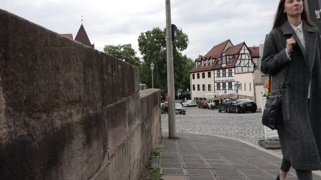 Woman in stylish coat walks down cobblestone street in historic European town
