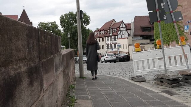Woman walks past construction barriers on a cobblestone street in historic town