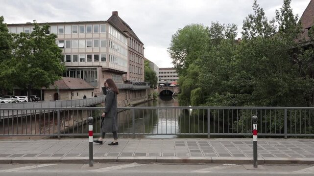 Woman walking across a bridge with modern buildings and trees in the background