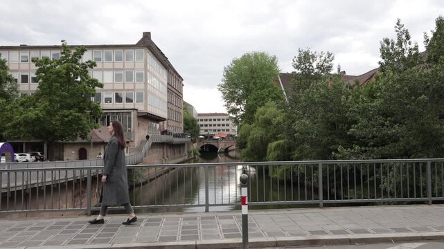 Woman in long coat walks across bridge over canal in European city