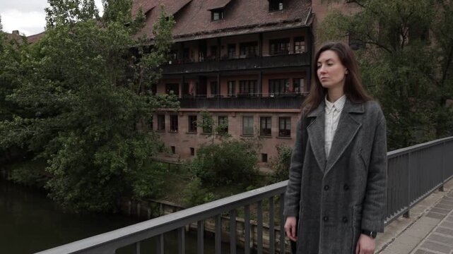 Woman in a coat standing on a bridge overlooking a historic building and river