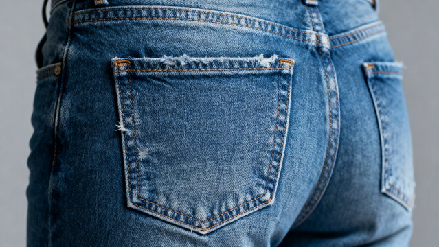 Close up back view of blue jeans highlighting detailed pockets, denim texture, stitching, fabric folds, casual urban style, worn appearance, and strong material structure showing realistic garment det