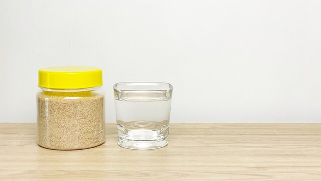 A jar of psyllium husk and a glass of water on a wooden surface against a neutral background. Concept for healthy eating, preparing a fiber-rich drink, and supporting digestion.