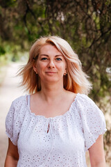 Naklejka premium A portrait of a positive, charming, and cheerful woman on a walk. A blonde woman in a white blouse looks at us. The blonde has a determined look. 