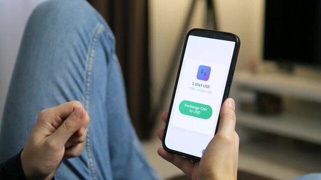 Viewing a currency exchange screen on a smartphone. The display shows a conversion rate of 0.0069 USD for 1 CNY. Perfect for fintech apps, foreign exchange, and digital banking visuals.