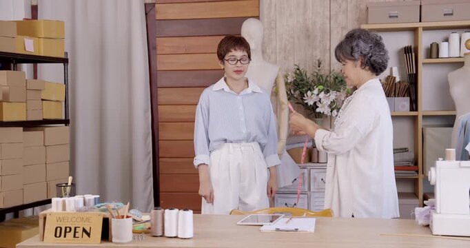 Asian customer holding tablet while senior seamstress giving advice during dressmaking consultation boutique fashion atelier tailoring couture fitting bespoke service small business craftsmanship