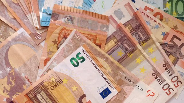 Various denominations of euro banknotes spread on white table surface.