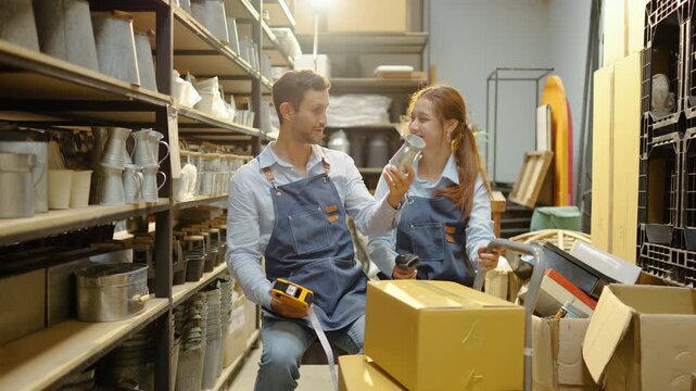 Two happy small business owners or warehouse workers checking inventory, scanning retail products, and packing cardboard boxes together in a store room, smiling and working efficiently as a team.