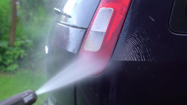 Washing car headlight with pressure washer outdoors. High pressure car wash. Car wash