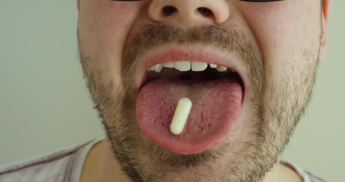 man placing a white pill on his tongue and swallowing it. Ideal for healthcare, medication, treatment, supplements, medical routines, pharmaceutical concepts, and wellness content.