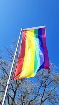 Rainbow pride flag waving in the wind against a blue sky