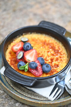 French cr&egrave;me br&ucirc;l&eacute;e dessert with fresh fruit served in a black bowl. Close-up of caramelized crust and elegant restaurant plating, perfect for gourmet dessert, fine dining, and food photography concep