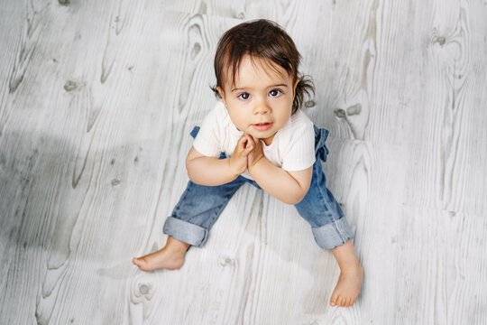 A sweet little girl is sitting on the floor in the living room.