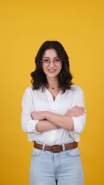 Young woman making silence gesture with finger on lips while smiling and looking around on yellow background. Vertical studio video ideal for secrecy, privacy, attention and communication concepts.