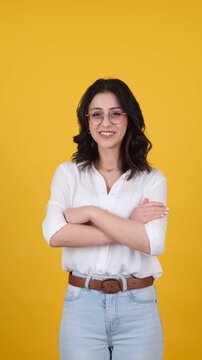 Caucasian happy young woman posing over yellow studio background, copy space. Pointing up with index fingers, show thumbs up ok gesture, arms crossed online offer approve concept idea vertical video.