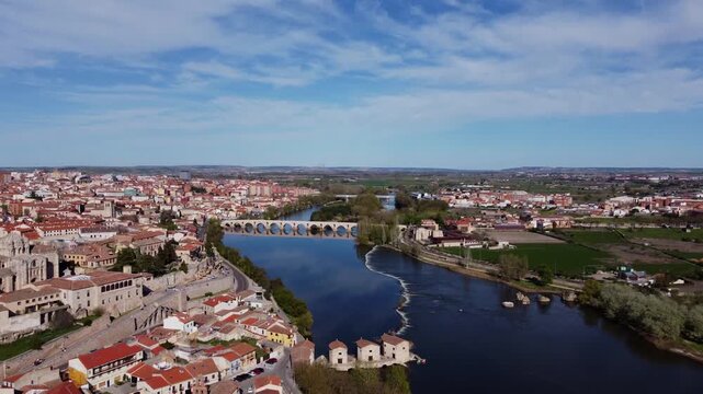 4K cinematic aerial drone shot flying over the Duero River, revealing the beautiful historic city of Zamora, Spain. Features the stone bridge, ancient walls, and old town on a bright sunny day.