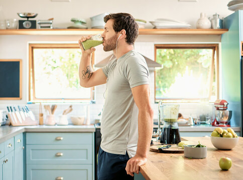 Wellness, earphones and man in kitchen with smoothie, organic juice and protein shake for gut health. Diet, person and audio tech in home with green drink, supplement and nutritional tips in podcast