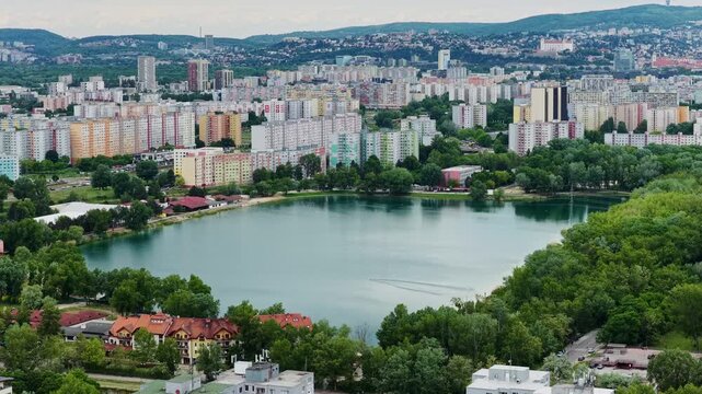 Aerial drone footage of Veľk&yacute; Draždiak lake surrounded by Petržalka residential district in Bratislava, Slovakia. Urban skyline, colorful apartment buildings and green summer landscape.