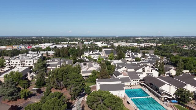 Aerial view flying over the San Joaquin Delta College campus, including buildings and the swimming pool complex, on a sunny day in Stockton, California with the city in the background