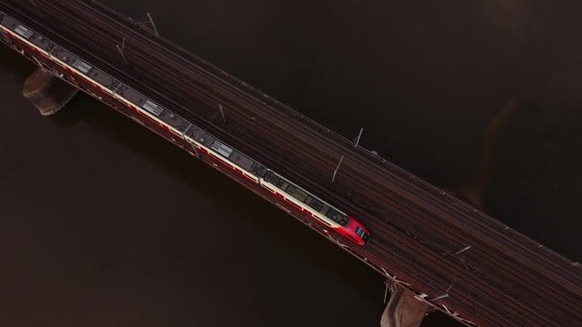 Aerial View Red Commuter Train Crossing Bridge Warszawa Over Dark River At Dusk, Empty Tracks And Maintenance Poles, Slow Commuter Journey, Urban Solitude, Minimalist Overhead Drone