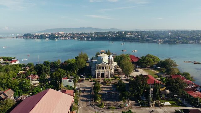 Dauis Church beside calm blue bay and tropical town in Bohol, drone approach to front