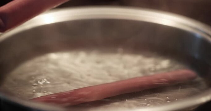 Close-up view of cooking hot dog meats in boiling and steaming metal pot with bubbling hot water.