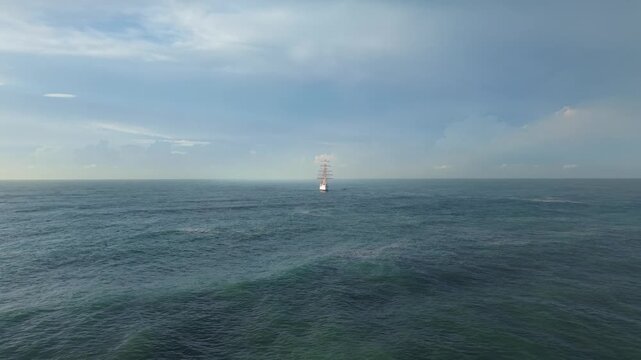 Aerial wide shot approaching a three-masted tall ship sailing on a calm, vast ocean under an expansive sky. Features smooth forward camera movement and maritime scale