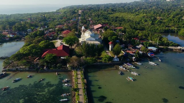 Dauis Church and tropical coastal village in sunny Bohol Philippines, drone pullback reveal from behind over waters