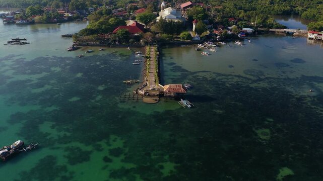 Long stone pier extending into clear coastal waters in Bohol, drone panoramic wide establishing from back to Dauis Church