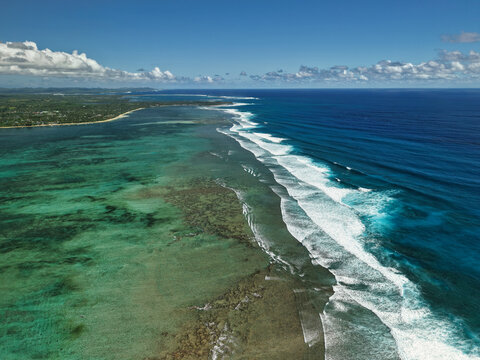 Aerial drone view of the reef break along Siargao Island, Philippines, where powerful ocean waves roll in and crash against the shallow coral reef.
