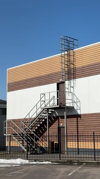 Modern building exterior with iron staircase, siding covered roof and metal ladder cage. Brown cladding over white wall