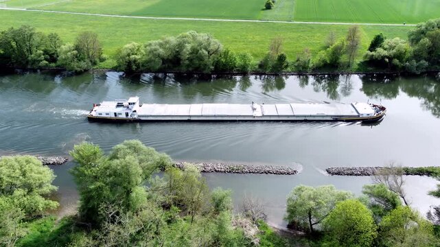 Drohne fliegt &uuml;ber Fluss mit Binnenschiff, Ufer mit Auwald und Agrarland, Luftaufnahme