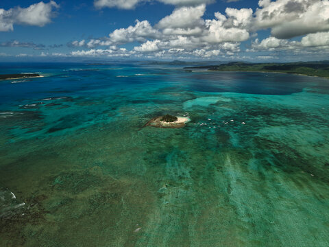Aerial drone view of Guyam Island, a small tropical island surrounded by vibrant turquoise waters and coral reefs near Siargao, Philippines.