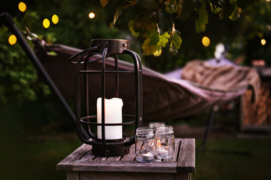 Hammock with lantern and fairy lights in evening garden setting. Cozy evening atmosphere with candlelight. Background for leisure and relaxation for outdoors.