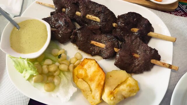 Close-up of traditional Peruvian dish Anticuchos served on a plate in a restaurant. Grilled marinated beef heart skewers with boiled potatoes and spicy sauces, authentic Peruvian cuisine. High quality