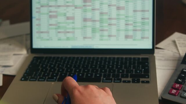 Close-up of a person working on financial data on a laptop with spreadsheet charts and calculator on desk. Budget planning, accounting and business analysis concept. High quality 4k footage