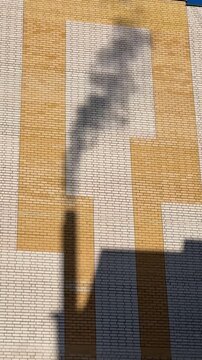 Shadow gas pipe smoke on brick facade under clear blue sky, sunlight casts dark silhouette and elongated pipe shadow