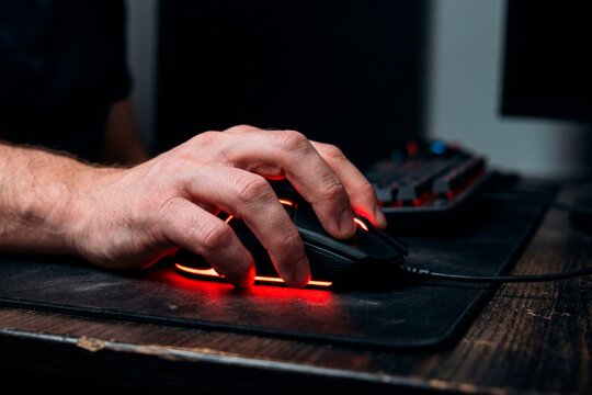 Primer plano de una mano tensa agarrando un rat&oacute;n de ordenador iluminado, concepto de frustraci&oacute;n tecnol&oacute;gica o ira digital.