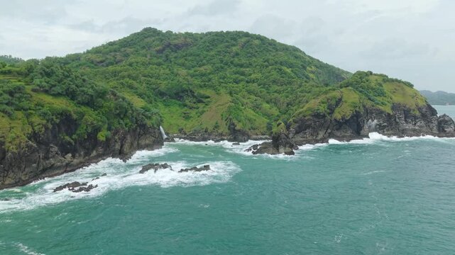 Aerial view of Banyutibo Water Fall cascading from lush green cliffs into the turquoise ocean with crashing waves Girisubo, Special Region of Yogyakarta, Indonesia.