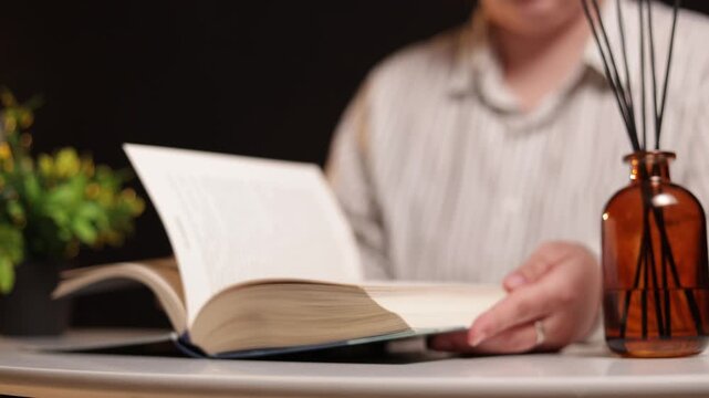 Person reading a book with an aroma diffuser and plant in soft lighting