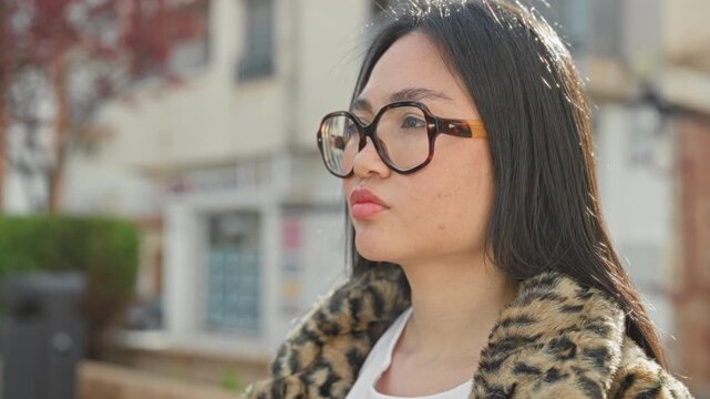 Woman with oversized tortoiseshell glasses and leopard fur coat gazes sideways, lips slightly pursed, on a street; quiet confidence.