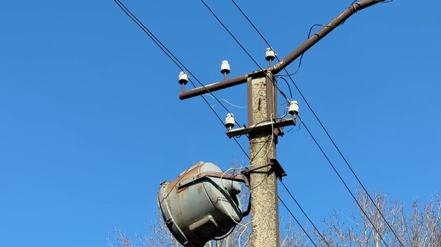 Spotlight on concrete pole, blue sky. Side view of large industrial light fixture hanging from utility pole, power wires crossing