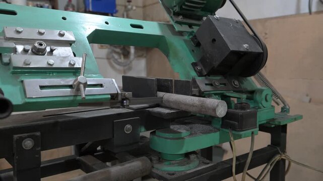 The lathe is in the production room. An electric metal cutting machine saws off a piece of metal with an automatic hacksaw to make a product