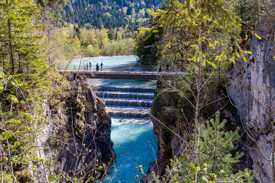 The magnificent Lechfall waterfall in F&uuml;ssen, a stunning multi-tiered turquoise cascade flowing through a narrow rock gorge with a pedestrian bridge and lush green forest, Bavaria, Germany.