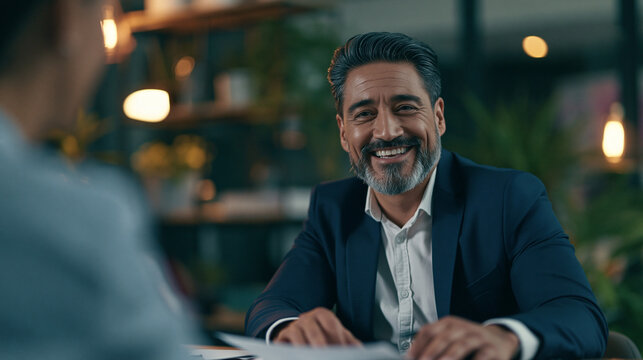 Hombre hispano sonriente y seguro de s&iacute; mismo, analista financiero, auditor, abogado o gerente de banco consultando a un cliente en una oficina moderna, concepto de negocio inmobiliario y de pr&eacute;stamos