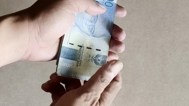 Close up of male hands collecting and counting fifty thousand Indonesian Rupiah banknotes