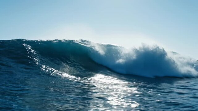 A towering wave crests, its foamy top contrasting against a clear blue sky