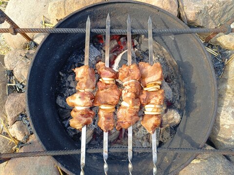 Top view of meat and onion skewers cooking over hot coals. Outdoor barbecue in a round metal fire pit surrounded by stones