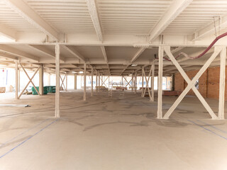 Fototapeta premium Wide angle photograph of a large commercial building interior under construction with steel pillars and beams covered in white fireproof spray coating and exposed concrete floor